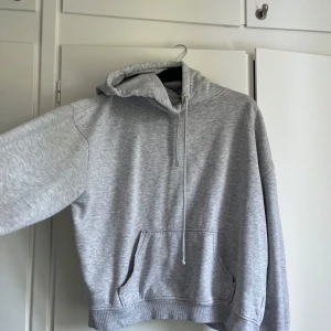 Ljusgrå hoodie - En stilren ljusgrå hoodie med klassisk magficka och snörning i huvan. Tröjan har en relaxed passform och är tillverkad i mjuk bomullsblandning, perfekt för chill dagar. Långa ärmar och ribbade muddar ger en skön vibe.