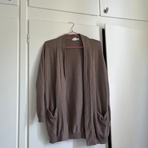 Beige kofta - Mjuk och enkel beige kofta från H&M BASIC i storlek S. Koftan är öppen framtill, har långa ärmar och två stora fickor. Perfekt att slänga på sig över en t-shirt eller linne. Materialet är tunt och stickat, vilket gör den skön att bära.
