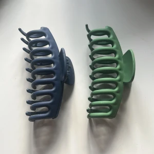 Två st hårklämmor - Säljer två rejäla hårklämmor i matta färger, en i mörkblått och en i dämpad grön. Båda har klassisk böjd form med breda taggar som håller håret på plats. Perfekta för att snabbt slänga upp håret i en snygg och enkel frisyr.