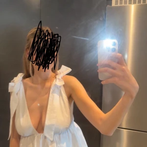 Vit omlottopp med rosett Zara S - Superfin vit omlottopp från Zara med djup v-ringning och breda axelband som knyts till stora rosetter på axlarna. Toppen har en luftig passform och är tillverkad i bomull, perfekt för varma dagar och en trendig look.