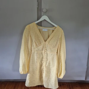 Gul kortklänning från Vila - Superfin gul kortklänning från Vila med broderade blommor, v-ringning och knappar framtill. Klänningen har långa puffärmar och smock i ryggen för en snygg passform. Storlek 36, skulle säga att den även passar er som är mellan storlek S-M. För er som är rädda att den blir för tight över bröstet så har jag 75D för referens. Använd någon enstaka gång, väldigt bra skick. 
