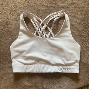 Vit sport bh - Superfräsch vit sporttopp från SOC med snygga korsade band i ryggen. Tillverkad i stretchigt material som andas, perfekt för träning😻Toppens design ger både stöd och stil, och den breda resåren nedtill håller allt på plats! Köpte fel storlek av en annan person, så aldrig använd av mig💕