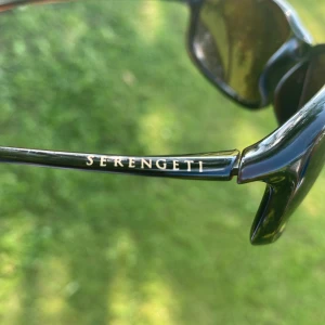 Svarta solglasögon från Serengeti - Snygga svarta solglasögon från Serengeti med rektangulära bågar och mörka linser. Bågarna är tunna och stilrena, perfekta för dig som vill ha en klassisk look med en modern touch. Lätta att bära och passar till de flesta outfits.