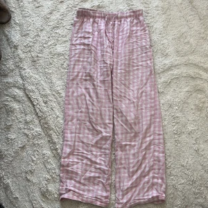 Rosa rutiga pyjamas byxor från Gina Tricot - Säljer ett par supermysiga byxor från Gina Tricot i rosa och vitt rutigt mönster. De har resår i midjan och är raka i modellen, perfekta för chill dagar hemma. Materialet är mjukt och skönt mot huden.