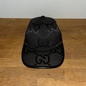 Svart Gucci Jumbo Keps - Svart Gucci jumbo keps från Gucci med ikoniskt GG-mönster över hela kepsen. Snygg och stilren accessoar som lyfter din outfit med lyxig känsla.