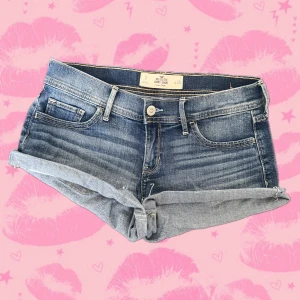 Blå lowrise short shorts jeansshorts från Hollister - Snygga blå vintage low rise short shorts mini shorts jeansshorts från Hollister med låg midja och uppvikta benslut. Klassisk femficksmodell med slitna detaljer och bakfickor med broderade sömmar. Materialet är mjuk bomull med lite stretch för extra komfort. Perfekta för varma dagar!