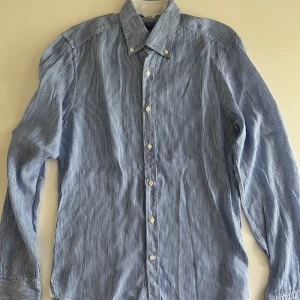 Randig blå skjorta från Stenströms - Säljer en slim fit skjorta från Stenströms i storlek S. Skjortan är blå med tunna vita ränder, har klassisk krage med knappar och långa ärmar. Tillverkad i linnen och bomull.