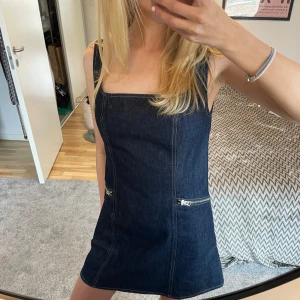 Mörk jeansklänning med dragkedjor - Oanvänd från samsoe samsoe, prislapp kvar! Nypris ca 2.500kr. Slutsåld och SÅ SNYGG!!!! Peerffeeekta sommarklänningen!!!  Snygg mörk jeansklänning med två dragkedjor framtill. Klänningen är ärmlös och har en stilren design som passar perfekt för en trendig look. 