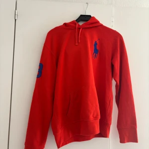 Röd hoodie från Ralph Lauren - Riktigt snygg röd hoodie från Ralph Lauren med stor blå logga på bröstet och siffran 3 på ärmen. Passad M och L