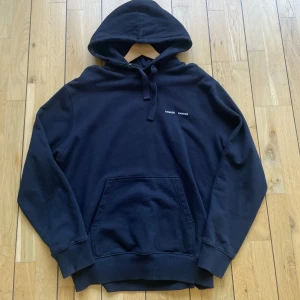 Mörkblå hoodie från Samsøe Samsøe - Säljer en mörkblå hoodie från Samsøe Samsøe i modellen Norsbro. Tröjan har huva med dragsko och en stor magficka framtill. Perfekt för en avslappnad stil och enkel att matcha med det mesta. S men passar L! 185-190 ungefär