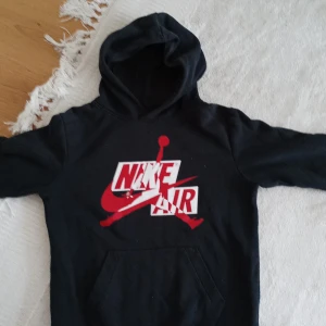 Svart Nike Air Jordan hoodie - Säljer en svart hoodie från Jordan med stor Nike Air-logga i rött och vitt på bröstet. Tröjan har huva och en klassisk känguruficka framtill. Perfekt för dig som gillar sportig streetstyle och vill ha något bekvämt och snyggt.