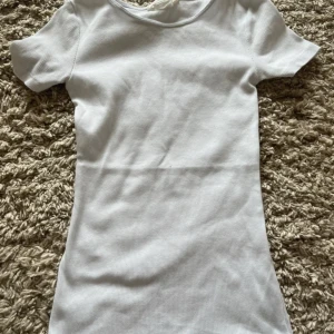 Vit ribbad t shirt från H&M - Säljer en enkel och stilren vit ribbad t shirt från H&M.   rund halsringning, perfekt för. Den är figurnära och gjord i ett mjukt, stretchigt material.