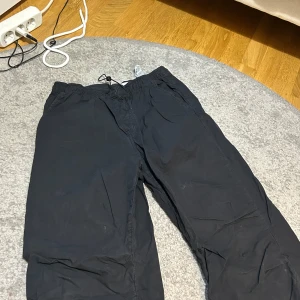 Svarta byxor med snörning från Zara - Svarta byxor från Zara med elastisk midja och justerbar snörning. Byxorna har raka ben och resår vid bensluten samt praktiska fickor både fram och bak. Perfekta för en avslappnad och stilren look.