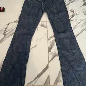 Low waist jeans - Säljer ett par klassiska blå utsvängda jeans med snygga broderade detaljer på bakfickorna. Byxorna har dragkedja och knapp framtill samt raka ben <3 DM om ni har frågor