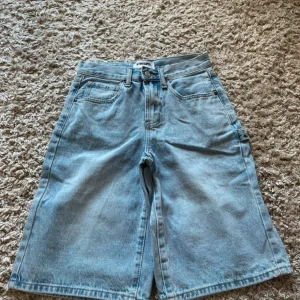 Ljusblå jeansshorts från RSQ - Säljer ett par ljusblå jeansshorts från RSQ med klassisk femficksdesign och gylf med dragkedja och knapp. Modellen är rak och lite längre, perfekt för en avslappnad stil. Passar dig som gillar denim och enkel design.
