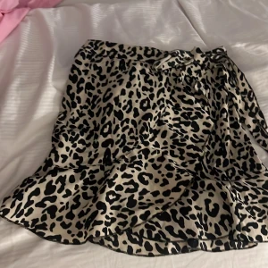 Leopardmönstrad kjol med volang från SHEIN - Säljer en snygg kort kjol från SHEIN med leopardmönster i svart och beige. Kjolen har volang nertill och knytband i midjan för extra detalj. Perfekt för dig som gillar djurmönster och vill sticka ut.