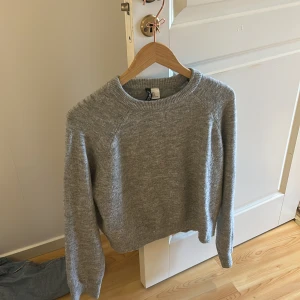 Grå stickad tröja från H&M - Säljer en enkel och stilren grå stickad tröja från H&M. Tröjan har rund halsringning och långa ärmar, perfekt för lager-på-lager under kyliga dagar. Passar till det mesta och är supermjuk och bekväm.