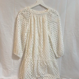 Vit broderad klänning med volang - Säljer en söt vit klänning med broderade blommor och hålmönster. Klänningen har trekvartsärm, volang nertill och en lös passform. Perfekt för sommarens alla tillfällen!