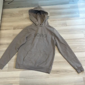 Hoodie från Björn Borg - Säljer en grå hoodie från Björn Borg. Tröjan har huva, magficka och långa ärmar. Perfekt för en avslappnad stil och enkel att matcha med det mesta.