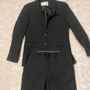 Svart kostym från Selected Homme - Säljer en stilren kostym från Selected Homme i nyskick, endast använd en gång vid min skolavslutning i nian. Byxorna är i storlek EU50 och kavajen i EU48. Kostymen är köpt för 1900 kr men säljs nu för 900 kr. Den är helt fri från fläckar eller skador. Perfekt för dig som går ut nian eller tar studenten och vill se stilig ut. Hör av dig vid intresse eller om du vill se fler bilder!