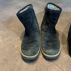Svarta fodrade boots med dragkedja i Gore-tex material - Svarta boots i mocka med mjukt grått foder och dragkedja på sidan. Skorna har en platt sula och är perfekta för kyligare dagar. Klassisk design med rund tå som tåler vatten samtidig som materialet andas.