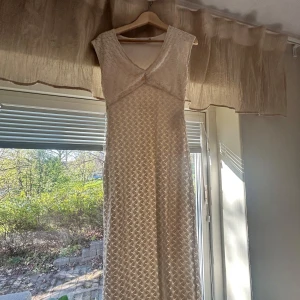 Vit långklänning med spets och v-ringning - Elegant vit långklänning med v-ringad hals och vackert spetsmönster över hela klänningen. Perfekt för speciella tillfällen när du vill känna dig extra fin. Klänningen har ärmlös design och en smickrande passform.