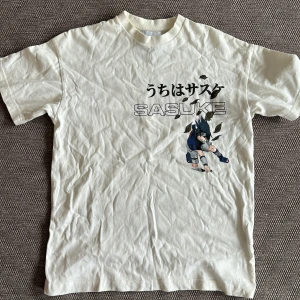 Vit t-shirt med Sasuke Uchiha-tryck från Naruto - Cool vit t-shirt med tryck av Sasuke Uchiha från Naruto på både fram- och baksidan. Japansk text och stor animegrafik gör den perfekt för fans av serien. Klassisk passform och rund hals.