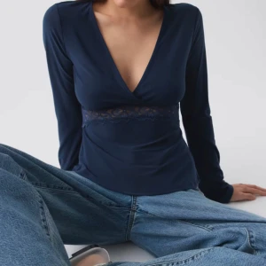 Mörkblå långärmad topp med spetsdetalj - Snygg mörkblå långärmad topp med djup v-ringning och spetsdetalj under bysten. Toppen har en figurnära passform och är perfekt att styla med jeans eller kjol. Materialet känns mjukt och stretchigt.