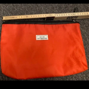 Röd necessär - Säljer en röd kuvertväska från Multi Bag i syntetmaterial. Väskan har svart dragkedja upptill och en enkel, stilren design. Perfekt för att organisera småsaker eller använda som necessär. Invändigt finns ett fack för extra förvaring.
