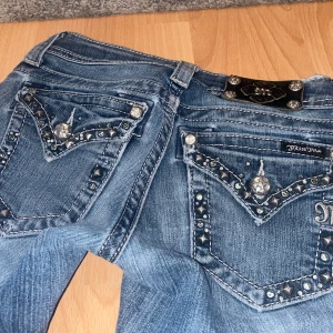 Blå Miss Me jeans med stenar och hål - (PRIS GÅR ATT DISKUTERAS) Säljer dessa blåa Miss Me jeansen med snygga detaljer som stenar och broderier på fickorna. Jeansen har bootcut-modell och låg midja, samt en slitning framtill. Är lite för långa för mig som är 149 och obs slitningen längst ner på ett av benen💗💗