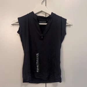 Svart ärmlös träningstopp med dragkedja  - Svart ärmlös träningstopp från Spartacus med kort dragkedja framtill och tryckt logga på sidan. Helt oanvänd men prislapp saknas.
