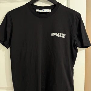 Svart t-shirt med tryck från Off-White - Svart t-shirt från Off-White med liten vit logga på bröstet och stort grafiskt tryck med texten 'WHT' och pilar på ryggen. Klassisk rund hals och korta ärmar. Perfekt för dig som gillar streetwear.
