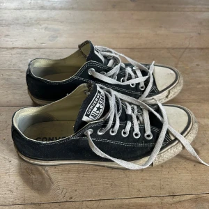 Svarta Converse All Star sneakers - Klassiska svarta Converse All Star sneakers med vit sula och vita snören. Skorna har rund tå, platt sula och tydliga logotyper på plösen och insidan. Perfekta för en avslappnad och tidlös stil.