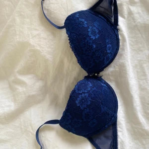 Mörkblå spets-bh från H&M - Säljer en mörkblå bh från H&M med vacker spets och blommigt mönster. Bh:n har vadderade kupor och justerbara axelband. Perfekt för dig som vill ha något både snyggt och bekvämt under kläderna.