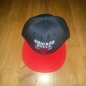 Chicago Bulls keps med röd skärm - Snygg keps med svart krona och röd skärm från Chicago Bulls. Framsidan har broderad logga och text. Perfekt för dig som gillar basket eller vill ha en sportig stil.