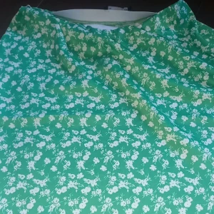 Grön blommig Kjol - Säljer en grön kjol med vitt blommigt mönster. Kjolen har en fräsch och somrig känsla med små vita blommor över hela tyget. Perfekt för varma dagar och midsommarfirande!