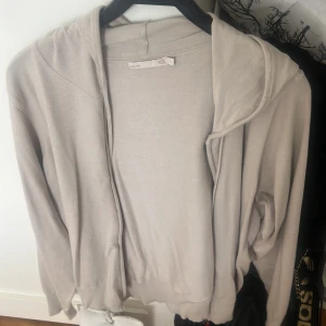 Beige tunn kofta med huva - Säljer en tunn och mjuk beige kofta från H&M med huva. Perfekt för lager-på-lager och enkel att matcha med olika outfits. Koftan har långa ärmar och är öppen framtill utan knappar eller dragkedja.