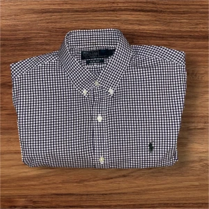 Rutig skjorta från Polo Ralph Lauren - Snygg långärmad skjorta från Polo Ralph Lauren i lila och vit rutig design. Klassisk button-down krage och broderad logga på bröstet. Perfekt till jeans eller chinos för en clean look. Perfekt 🤩 till sommaren! Hör av dig vid frågor eller prisförslag. 