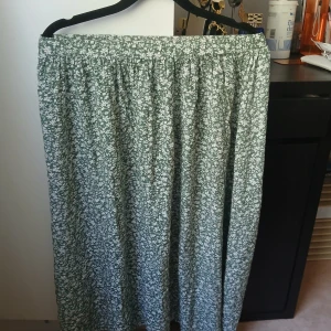 Grön blommig långkjol - Säljer en grön långkjol med vitt blommigt mönster från Born to dress kids. Kjolen har en avslappnad passform och resår i midjan för extra komfort. Perfekt för dig som gillar en luftig och somrig stil.