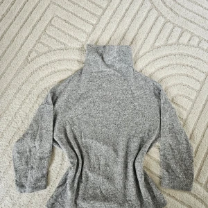 Grå polotröja i mjukt material - Säljer en grå polotröja med lång ärm och hög krage. Tröjan är i ett mjukt och stretchigt material. Enkel och stilren design som passar till mycket.