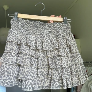 Leopardmönstrad volangkjol - Säljer en kort volangkjol med leopardmönster i beige och grå toner. Kjolen har flera lager volanger och en smockad midja som ger en bekväm passform. Perfekt till sommarn som topp eller kjol😍😍😍