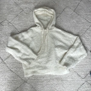Vit fluffig hoodie från H&M - Mysig vit hoodie från H&M i fluffigt material. Tröjan har huva med dragsko och långa ärmar. Perfekt för kyliga dagar när du vill vara både bekväm och snygg.
