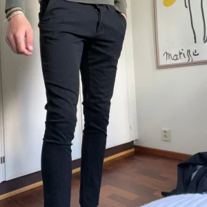 Svarta kostymbyxor från Tailored Originals - Snygga svarta kostymbyxor från Tailored Originals med skinny passform och raka ben. Byxorna har diskreta fickor och stängs med dragkedja och knapp. Perfekta för en stilren look.