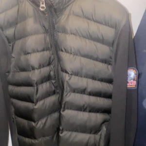 Svart hybridjacka från Parajumpers cardigan  - Säljer en svart hybridjacka från Parajumpers med quiltad front och rygg i pufferstil samt ärmar i mjuk bomull. Jackan har dragkedja och klassisk PJS-logga på ärmen. 