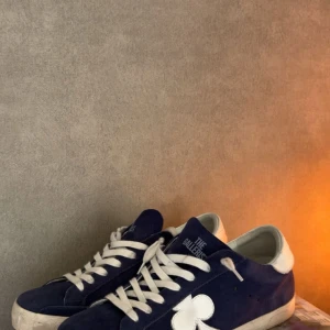 Mörkblå sneakers från The Gallerist - Säljer ett par mörkblå sneakers från The Gallerist med vita snören och en vit fyrklöverdetalj på sidan. Skorna knappt använda, så dem är i nyskick hör av er vid frågor osv.