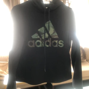 Svarta träningsbyxor från Adidas med kamouflagedetaljer - Säljer ett par svarta träningsbyxormed tillhörande tröja  från Adidas med klassisk logga på låret och coola kamouflagedetaljer längs sidorna. Byxorna har resår i midjan och smal passform nertill. Perfekta för gymmet eller chill.