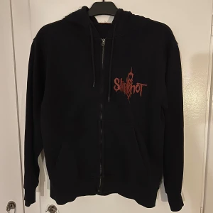 Slipknot hoodie/huvtröja - Snygg Slipknot hoodie köpt för ungefär 500 på Blue Fox i Stockholm för ett par år sen. Säljer den då jag ej lyssnar på bandet mer. Lappen är bortklippt men har sparat den så jag skickar med den också! ❤️ Osäker på storlek då det inte står och jag har glömt, men jag bär själv stl xs/s så skulle säga att den är ungefär stl M/L på kvinnor och stl S/M på män! :) Katt finns i hemmet och det är tyvärr hon som har bitit på trådarna lol. 