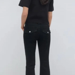 Svarta Lågmidjade jeans - Snygga svarta jeansbyxor med en klassisk design. Byxorna har en rak passform och är perfekta för en stilren look. De har fickor med knappar baktill och en bekväm midja.