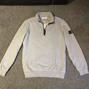 Grå tröja från Stone Island Junior - Säljer en stilren grå tröja från Stone Island Junior. Tröjan har en halv dragkedja och ett ikoniskt märke på ärmen. Helt äkta med tag och äkthetsbevis. Nypris 1750kr, säljes för 599. Storlek 14Y, typ som xs/s. Aldrig använd.
