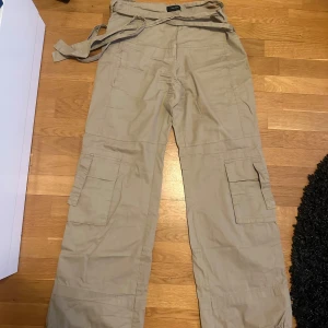 Beige cargobyxor med knytband - Snygga beige cargobyxor med praktiska fickor och knytband i midjan. Perfekta för en avslappnad stil med en loose passform. Byxorna har flera fickor för extra förvaring och är tillverkade i ett bekvämt material.
